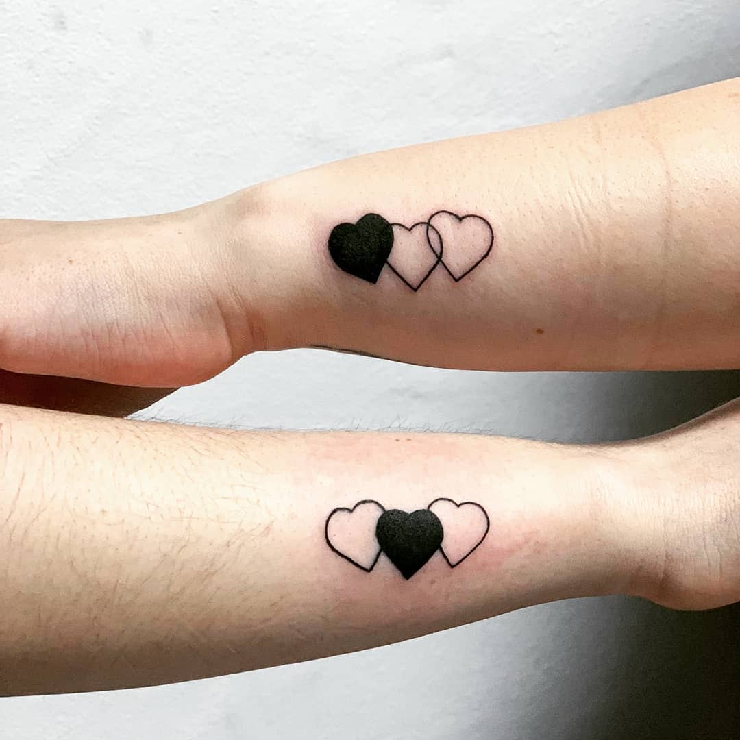 Two forearms with matching tattoos of three interlocking hearts, one solid black and two outlined